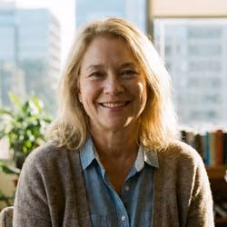 Porträt einer Frau mittleren Alters, lächelnd, sitzt in heller Umgebung. Ruhige, professionelle Ausstrahlung. Klassisches Autoren-/Redaktionsportrait.