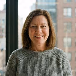 Porträt einer Frau mittleren Alters, lächelnd, sitzt in heller Umgebung. Ruhige, professionelle Ausstrahlung. Klassisches Autoren-/Redaktionsportrait.